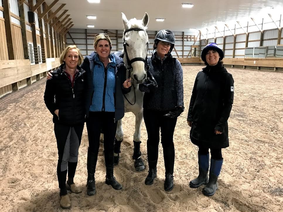 Women posing with a dressage horse in an indoor arena.